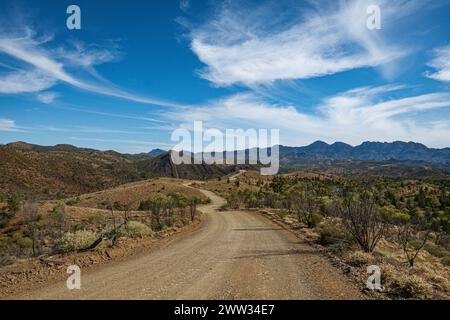 Route de gravier menant à travers l'outback avec des montagnes en toile de fond. Banque D'Images