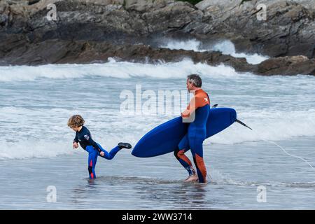 Un père et son jeune fils pataugant dans la mer avec une planche de surf à Fistral à Newquay en Cornouailles au Royaume-Uni. Banque D'Images