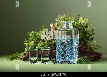 Gin bleu en carafe sur un fond de vieux accrocs et de branches de genévrier avec des baies. Fond vert avec espace de copie. Banque D'Images