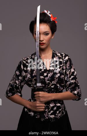 Femme asiatique, mode et épée en studio sur confiance avec fond gris, style traditionnel et élégant. Portrait, japonais et femme personne avec Banque D'Images