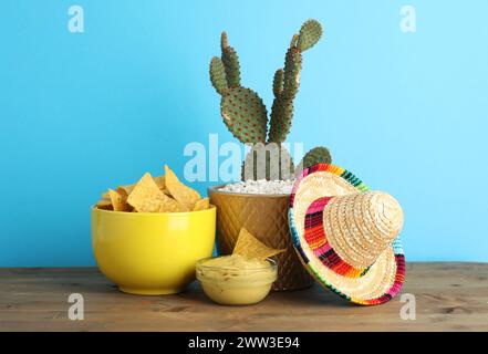 Chapeau sombrero mexicain, cactus, croustilles de nachos et guacamole dans des bols sur une table en bois sur fond bleu clair Banque D'Images