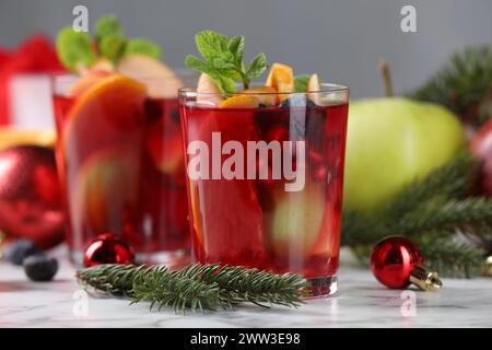 Boisson aromatique de Sangria dans des verres, des ingrédients et un décor de Noël sur une table en marbre blanc Banque D'Images