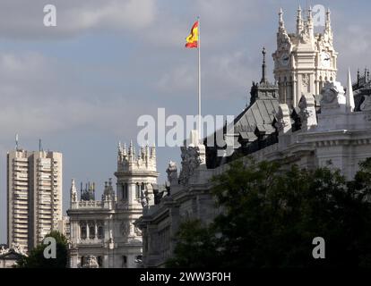 Drapeau espagnol flotte au-dessus de l'architecture opulente sous un ciel nuageux Madrid Espagne bâtiment postal Banque D'Images