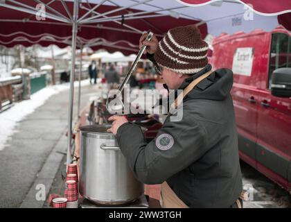 Lanslevillard, France, 10 janvier 2024 : un vendeur remplit une tasse de vin chaud sur le marché de la ville Banque D'Images