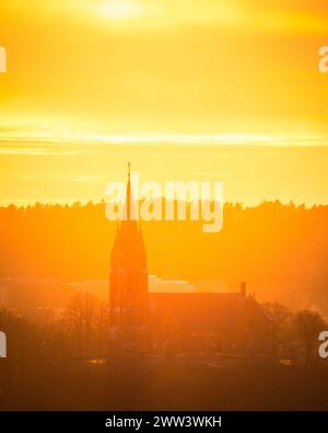 Le soleil couchant baigne le paysage dans une lueur chaude et dorée, avec la silhouette d'un clocher d'église s'élevant bien en évidence sur le fond radieux Banque D'Images