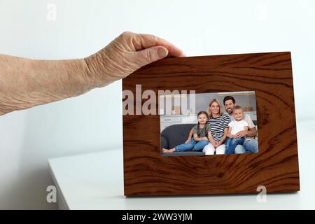 Femme âgée avec portrait photo encadré de sa famille à l'intérieur, gros plan Banque D'Images
