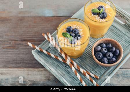 Smoothie à la mangue rafraîchissant et sain dans des verres avec des flocons de noix de coco et des bleuets frais sur fond de bois Banque D'Images