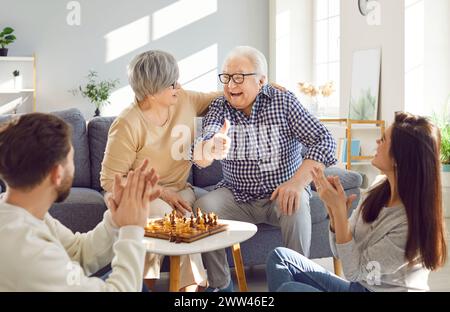 Heureux vieux parents âgés jouant aux échecs avec des enfants adultes assis à table dans le salon à la maison Banque D'Images