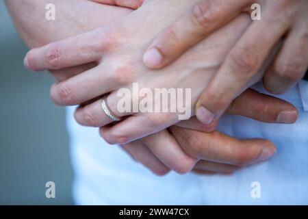 Une photo en gros plan capturant le toucher délicat des mains d'un couple serrées ensemble, avec un focus sur une bague en diamant qui signifie un engagement profond. L’image évoque un sentiment d’intimité et le lien tendre partagé entre les partenaires. Étreinte douce des mains avec un aperçu d'une bague en diamant. Photo de haute qualité Banque D'Images