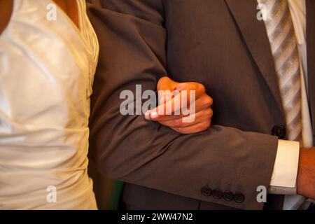 La photographie se concentre sur les mains entrelacées d'une mariée et de son père, symbolisant le lien affectueux qu'ils partagent. Le contraste de la délicate robe de satin de la mariée et le costume formel de son père ajoute à la profondeur émotionnelle de la journée. Moment tendre entre mariée et père le jour du mariage. Photo de haute qualité Banque D'Images