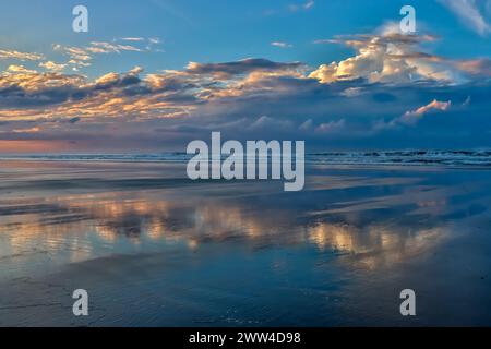 Image tôt le matin de nuages et de ciel reflétant la plage humide et l'eau peu profonde à marée basse. Banque D'Images