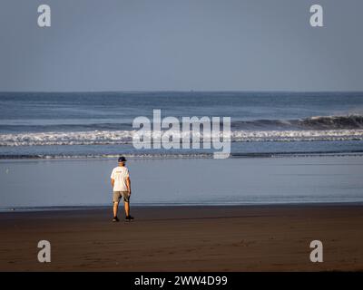 Un homme âgé marchant seul sur une plage déserte tôt le matin près du bord de l'eau. Banque D'Images