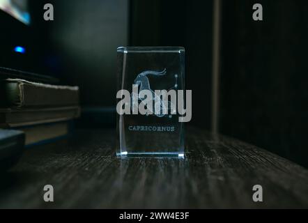 Figurine transparente en verre sur fond sombre avec l'image du Capricorne et l'inscription. Horoscope, astrologie et isotères Banque D'Images