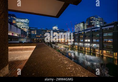 Londres, Royaume-Uni : vue nocturne du domaine Barbican dans la ville de Londres avec lac et fontaines. Un exemple éminent de l'architecture brutaliste. Banque D'Images