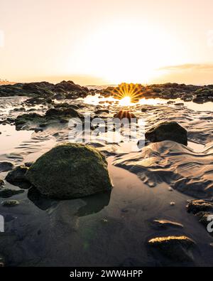 Une vue verticale d'un coucher de soleil sur une plage rocheuse avec la lumière du soleil se reflétant sur l'eau Banque D'Images
