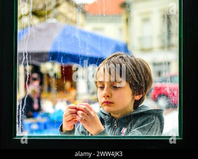 Jeune garçon regardant les doigts à travers la fenêtre striée de pluie - Preuilly-sur-Claise, , Indre-et-Loire (37), France. Banque D'Images