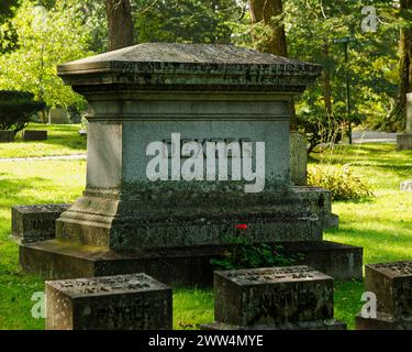 2023 - cimetière de Lowell - Lowell, ma. Un grand monument portant le nom DE DEXTER entouré d'un riche feuillage vert avec une fleur rouge vif dans le foregro Banque D'Images