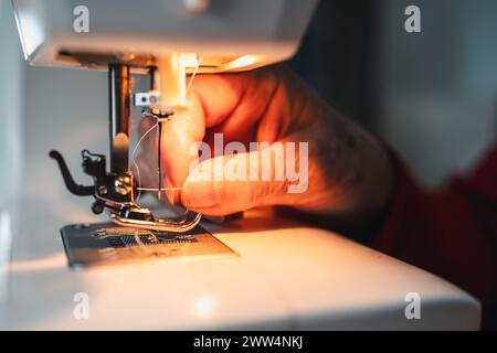 détail des doigts de femme enfilant l'aiguille de machine à coudre avec du fil à coudre Banque D'Images