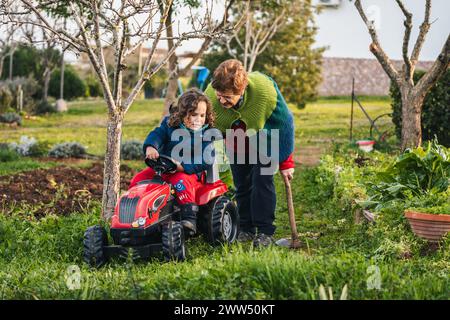 grand-mère et petit-fils jouant avec un tracteur dans le jardin à la maison Banque D'Images