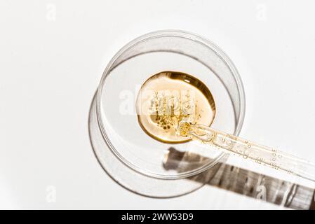 Échantillon de sérum de visage de rétinol dans une boîte de Pétri gros plan sur fond blanc. Compte-gouttes pour pipette d'huile de face. Texture de produit cosmétique pour le visage de beauté, rese de soins de la peau Banque D'Images