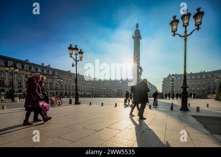 Silhouettes de piétons marchant dans la chaleur d'un soleil couchant à la place Vendôme, Paris. Banque D'Images