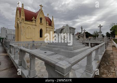 099 ensemble de statues sur des piédestaux surplombant des tombes, panthéon néo-gothique jaune, cimetière Cementerio de Colon, avenue principale côté est. La Havane-Cuba. Banque D'Images