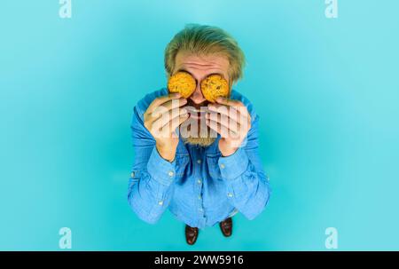 En-cas sucré. Homme barbu couvert les yeux de délicieux biscuits à l'avoine. Beau mâle tenant des biscuits biscuit avec des pépites de chocolat. Petit déjeuner ou déjeuner Banque D'Images