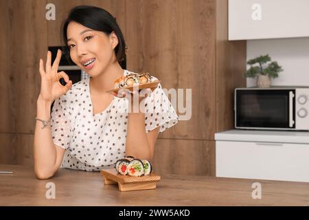 Jolie jeune femme asiatique avec de savoureux rouleaux de sushi montrant OK dans la cuisine Banque D'Images