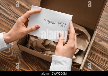 Femme mettant la lettre DE REMERCIEMENT dans le paquet de carton sur la table en bois Banque D'Images