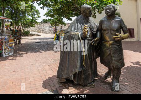 Cartagena, Colombie - 25 juillet 2023 : statue de San Pedro Claver parlant à un local sur sa place. Stand de vendeur de rue vendant des souvenirs et foli vert Banque D'Images