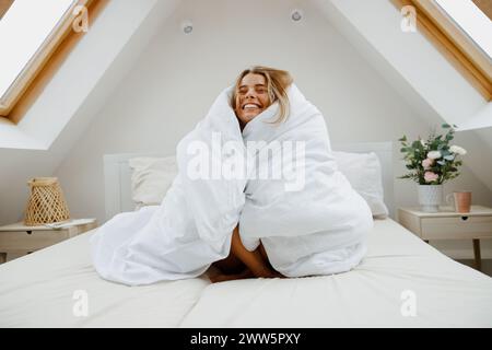 Femme en couverture blanche assise sur le lit entourée de plantes d'intérieur pour le confort Banque D'Images