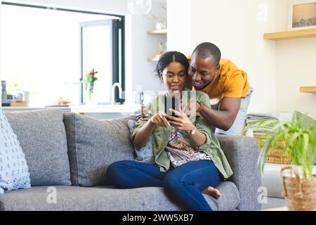 Un couple diversifié utilise un smartphone avec un espace de copie sur le canapé à la maison Banque D'Images