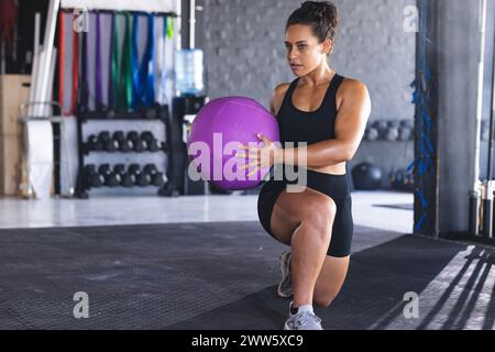 Une jeune femme hispanique en forme s'entraîne avec un medecine ball violet avec un espace de copie dans une salle de gym Banque D'Images