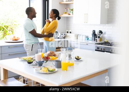 Un couple diversifié partage un moment dans une cuisine ensoleillée à la maison au petit déjeuner Banque D'Images