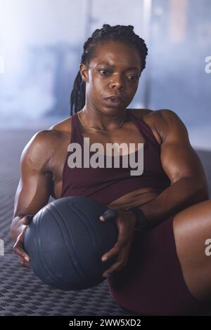 Une femme afro-américaine d'âge moyen forte tient un medicine ball dans la salle de gym Banque D'Images