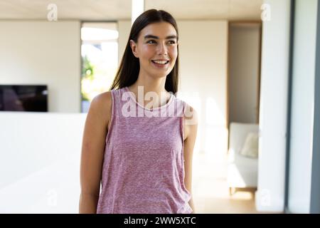 Une jeune femme brune caucasienne se tient souriante dans une pièce lumineuse à la maison Banque D'Images