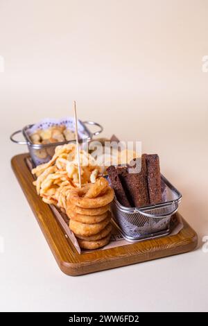 Plateau de bière vue de dessus avec croûtons, rondelles d'oignon, frites sur une planche de bois. Banque D'Images