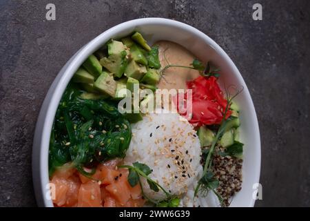 Vue de dessus des ingrédients frais pour un bol de poke sain avec saumon, avocat, concombre, germes, riz, et sésame sur assiette blanche Banque D'Images