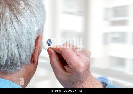 Plan américain d'adaptation d'une prothèse auditive à une personne âgée aux cheveux blancs, vue arrière. Banque D'Images