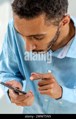 Jeune homme ajustant l'intensité du volume de l'aide auditive avec le smartphone. Banque D'Images