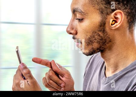 Jeune homme ajustant l'intensité du volume de l'aide auditive avec le smartphone. Banque D'Images