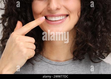 Jeune femme montrant ses dents avec une bande blanchissante sur fond gris clair, gros plan Banque D'Images