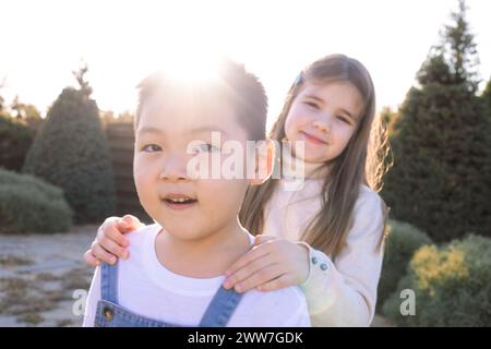 Deux petits enfants de races différentes jouent dans le jardin en plein air. Un garçon asiatique et une fille caucasienne s'amusent ensemble dans la cour o Banque D'Images