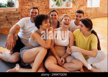 Les gens souriants multiraciaux s'assoient sur des tapis après avoir fait du yoga au club de fitness. Groupe de jeunes athlètes de différents âges et nationalités se détendre et se reposer à l'arrière Banque D'Images