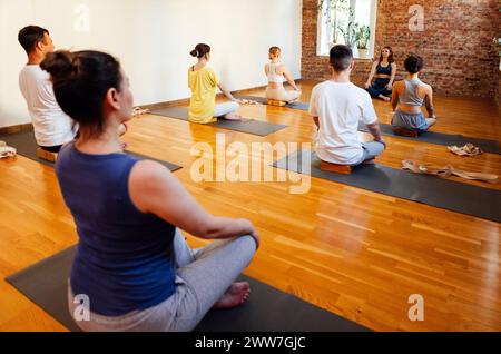 Les personnes athlétiques de différents âges et races pratiquent les asanas de yoga avec un entraîneur. Jeunes femmes et hommes sportifs multiethniques assis les jambes croisées sur des tapis et des s Banque D'Images