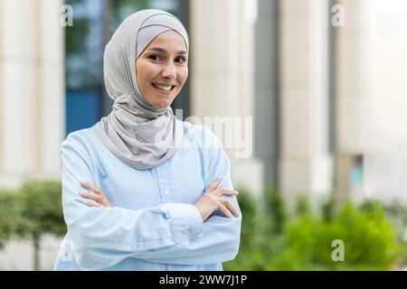 Portrait d'une femme musulmane joyeuse portant un hijab, debout avec confiance, les bras croisés dans un cadre urbain. Banque D'Images