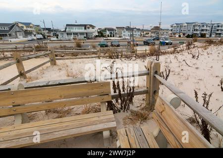 Un paysage serein montrant des maisons côtières bordées derrière des dunes de sable, clôturées par une clôture en bois, capturant l'essence tranquille de la vie côtière. Banque D'Images