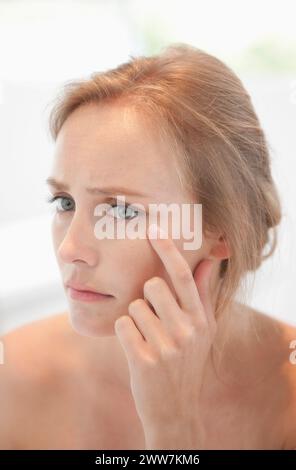 Femme au miroir concernés contrôle son visage Banque D'Images