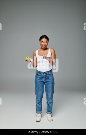 heureuse femme afro-américaine comparant les suppléments avec fond gris pomme vert, vitamines Banque D'Images