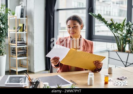 diététiste afro-américaine concentrée sur l'enveloppe près des suppléments sur son bureau de travail Banque D'Images